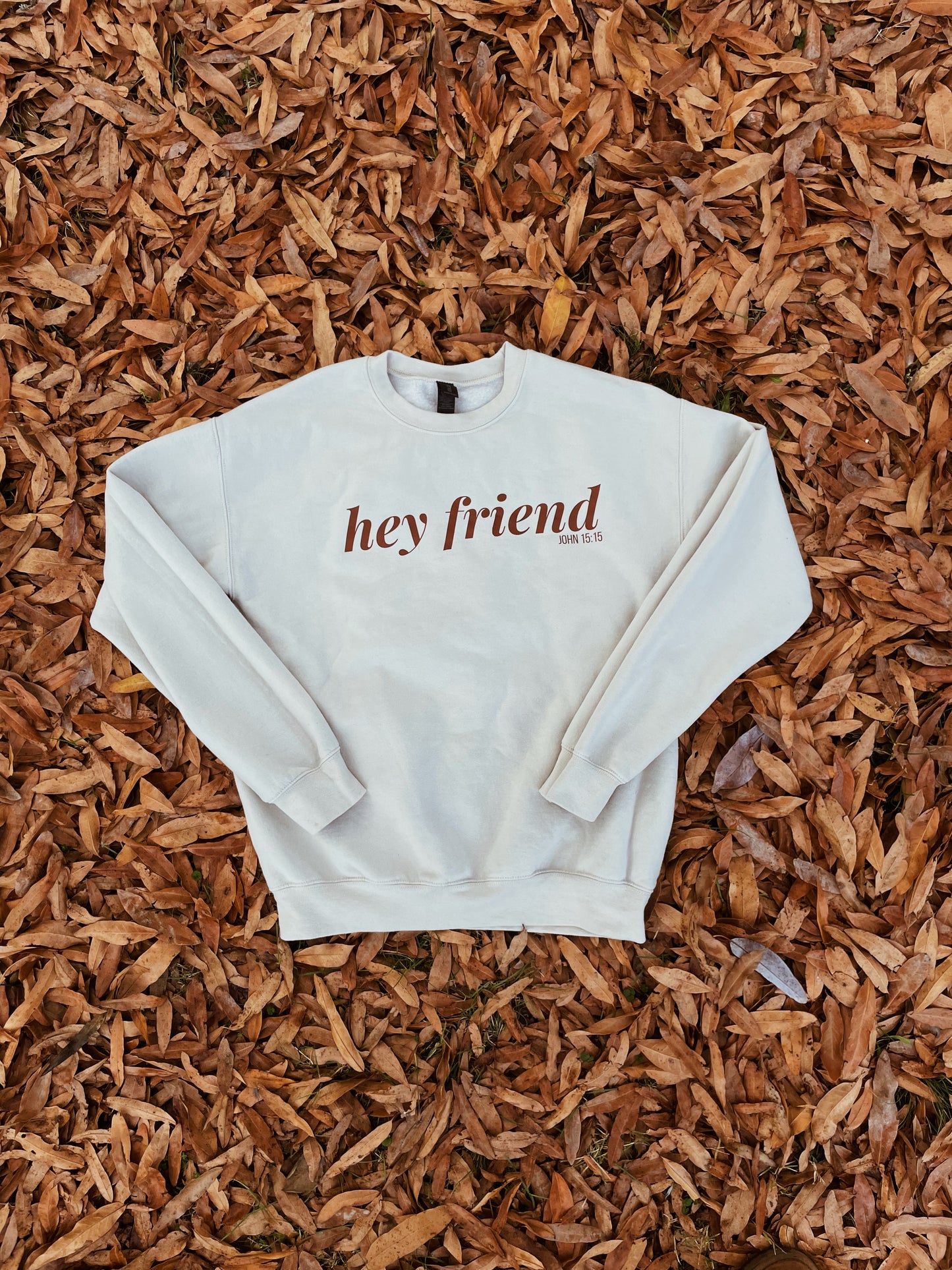 white sweatshirt with 'hey friend' text on a bed of wood chips